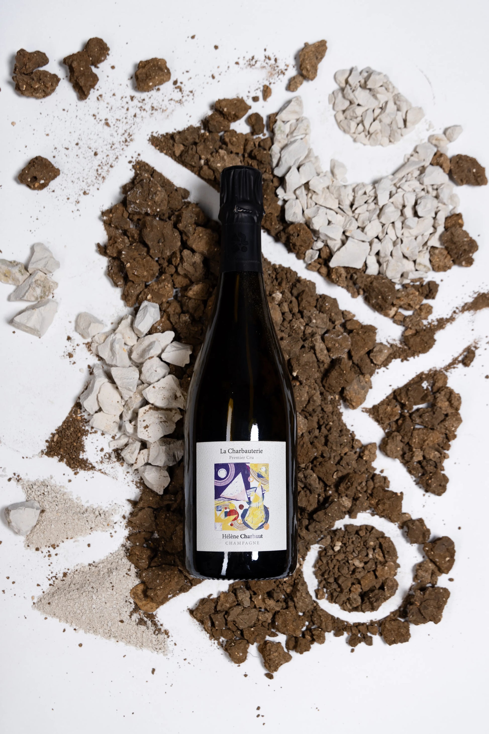 Eine Flasche des Winzerchampagners La Charbauterie von Hélène Charbaut wird umrahmt von Kalk- und Kreidesteinen die den Boden repräsentieren sollen auf dem die Trauben wachsen.